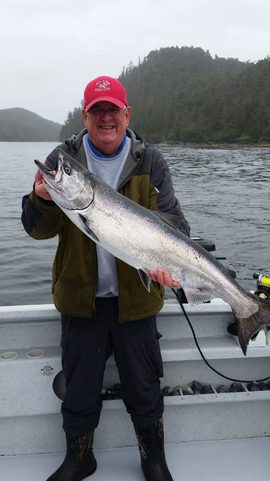 Angler holding a bright king salmon with forested shoreline in the background.