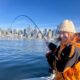 Angler smiling while fighting a fish in front of the Seattle skyline on a calm Puget Sound morning