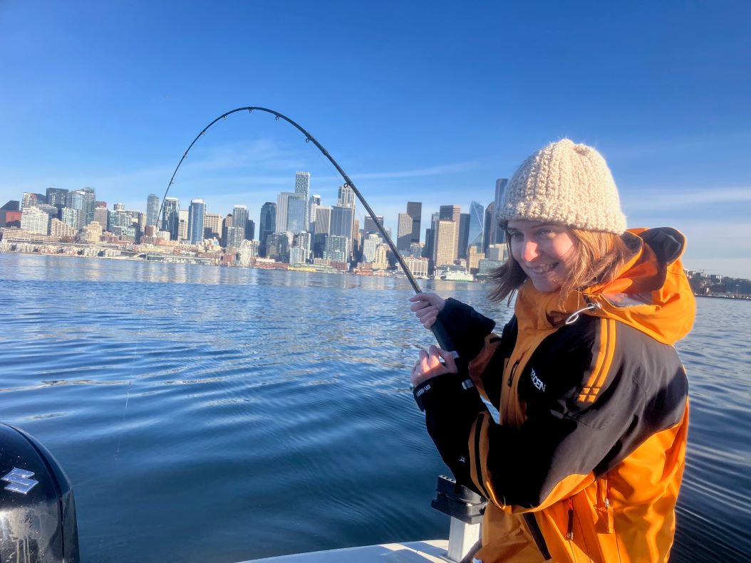 Angler smiling while fighting a fish in front of the Seattle skyline on a calm Puget Sound morning